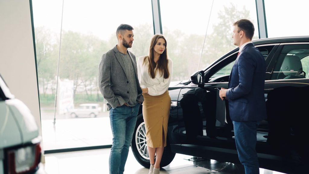 A couple converses with a salesperson about buying a car inside a dealership.